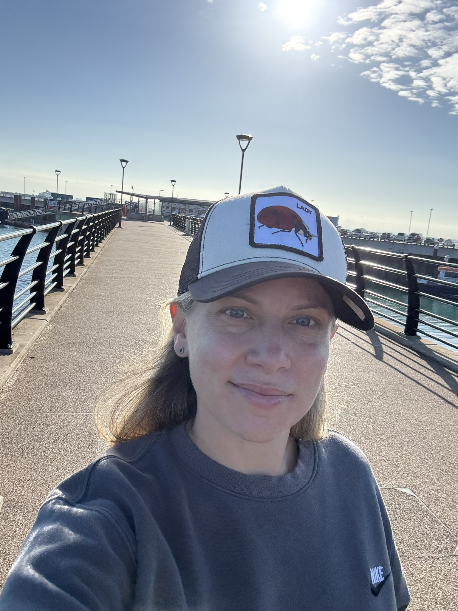 Tamsin in a baseball cap on a sunny pier, looking back at the camera